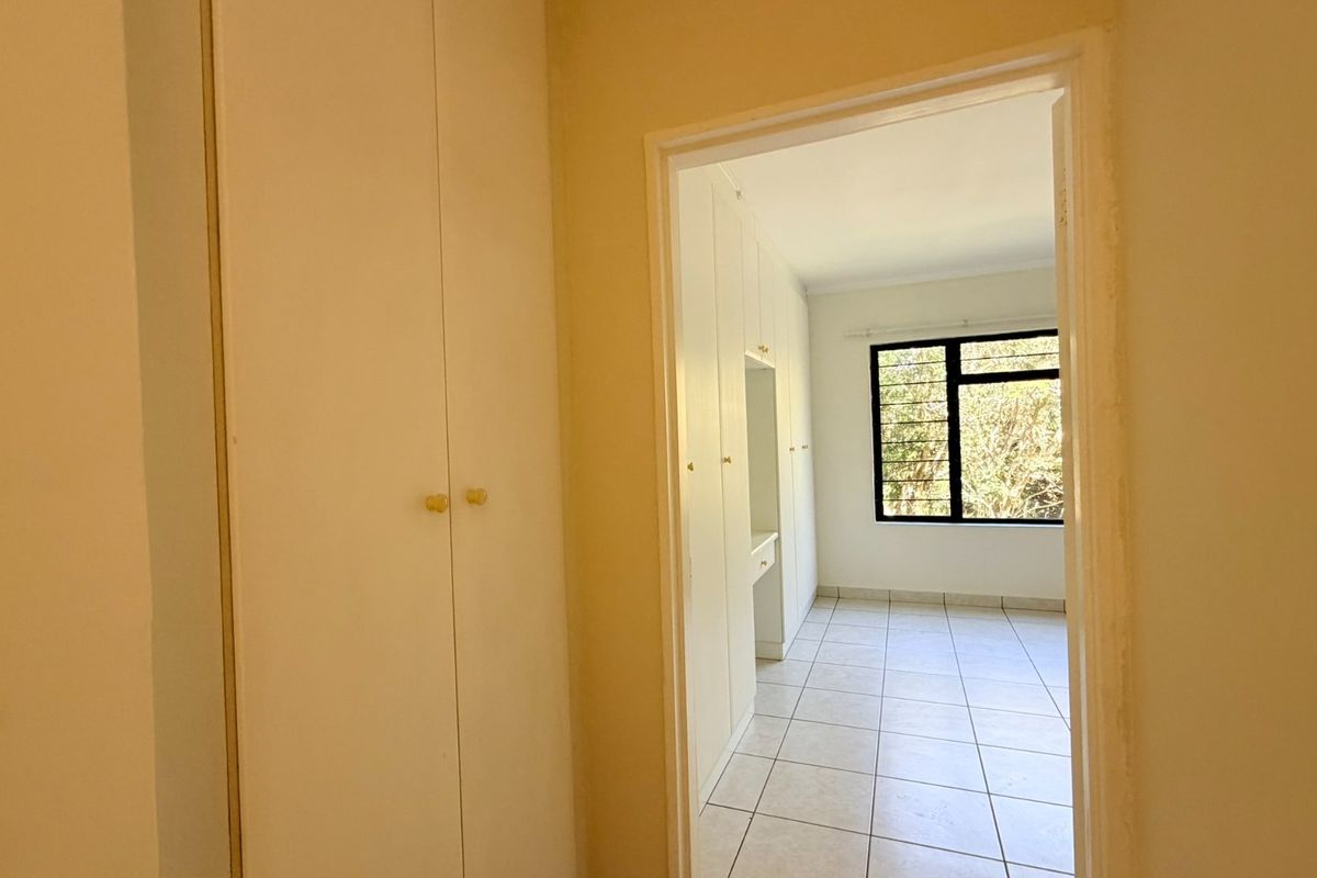 A bright, empty bedroom featuring tiled flooring, built-in cupboards, and a window with security bars, offering a clean and functional living space.