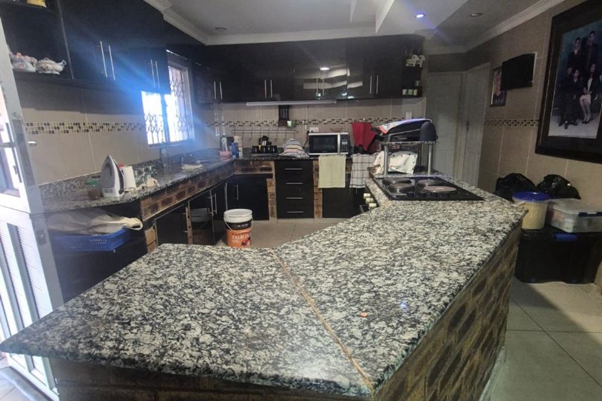 A spacious kitchen featuring dark cabinetry, granite countertops, and a unique exposed brick breakfast bar with integrated cooktop and tiled flooring.