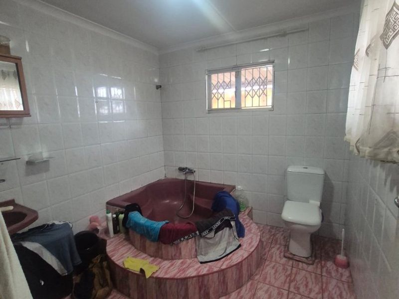 A dated bathroom featuring a sunken bathtub, tiled walls and flooring, and a standard toilet. The space would benefit from modern updates.