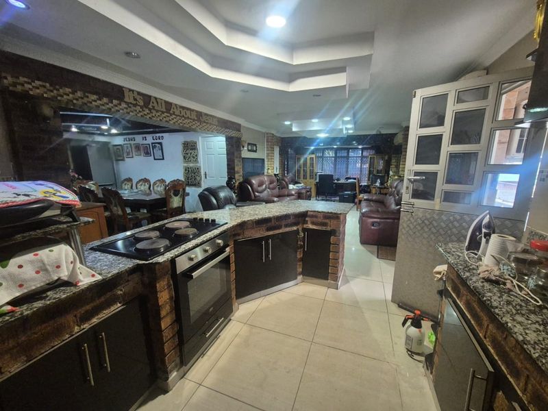 Open-plan kitchen and living area featuring a brick-base island with granite countertops, built-in oven, electric hob, and recessed ceiling lighting.