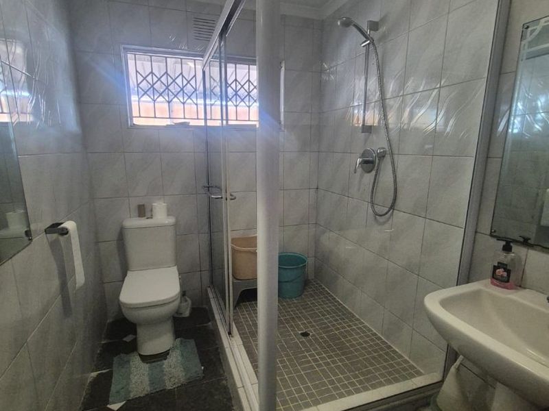A functional bathroom featuring a glass-enclosed shower, pedestal basin, and toilet with tiled finishes throughout.