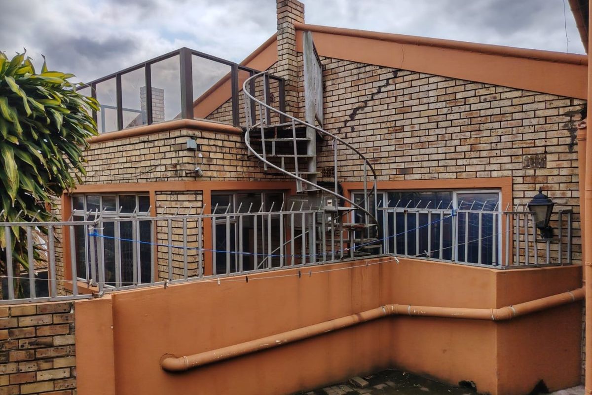 Rear exterior view featuring a brick facade, a metal spiral staircase leading to an upper balcony, and paved patio area with security fencing.