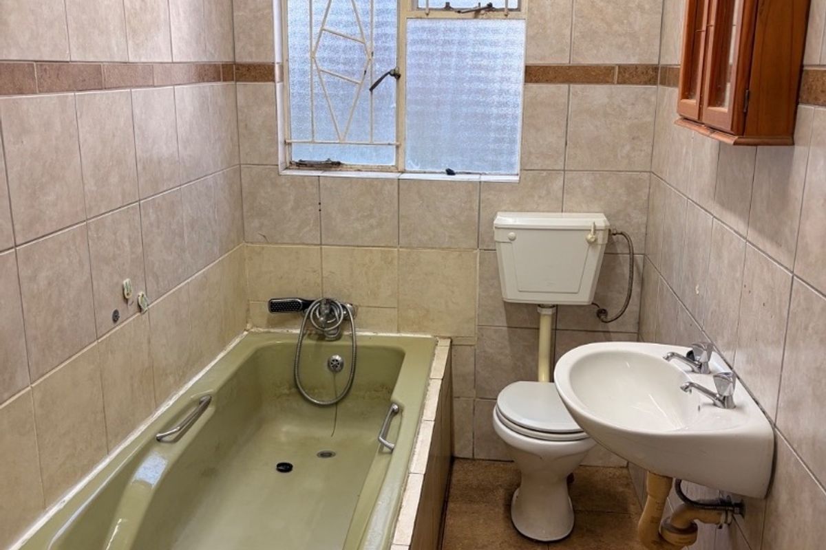 A dated bathroom featuring a built-in bathtub, wall-mounted basin, and toilet, finished with neutral wall and floor tiles.