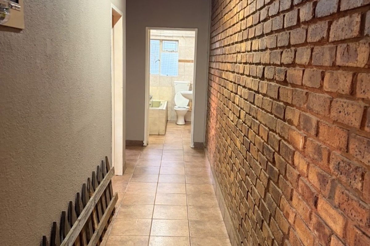 A long hallway featuring an exposed brick feature wall and tiled flooring, leading towards a bathroom.