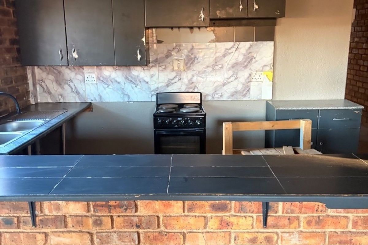 A dated kitchen featuring a brick breakfast bar, tiled countertops, and dark cabinetry in need of refurbishment.
