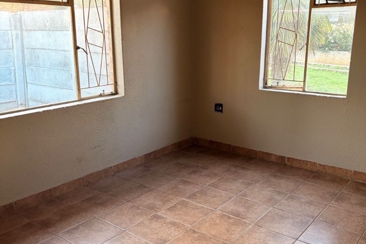 An empty bedroom featuring tiled flooring, steel-framed windows with security bars, and neutral wall finishes, offering a blank canvas for potential updates.