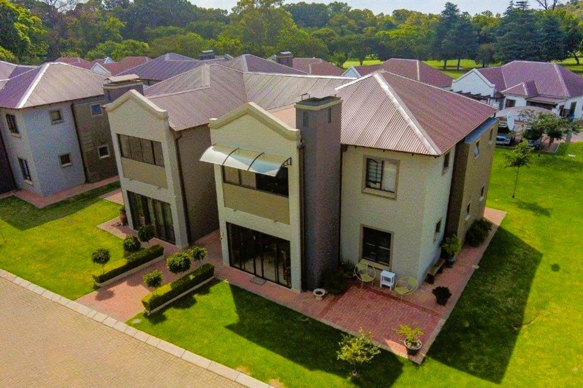 Aerial view of a multi-unit residential property featuring metal roofing, brick paved patios, and well-maintained surrounding lawns within a landscaped estate.