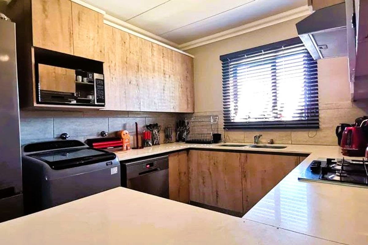 Modern kitchen featuring wood-finish cabinetry, stone countertops, integrated appliances, a gas hob, and a tiled backsplash with ample storage space.
