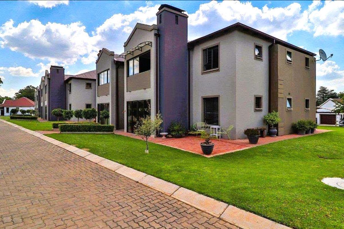 Rear view of a multi-story residential building featuring a brick paved patio area, well-maintained lawn, and paved driveway access.