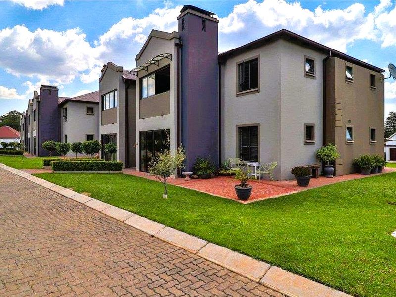 Rear view of a multi-story residential building featuring a brick paved patio area, well-maintained lawn, and paved driveway access.