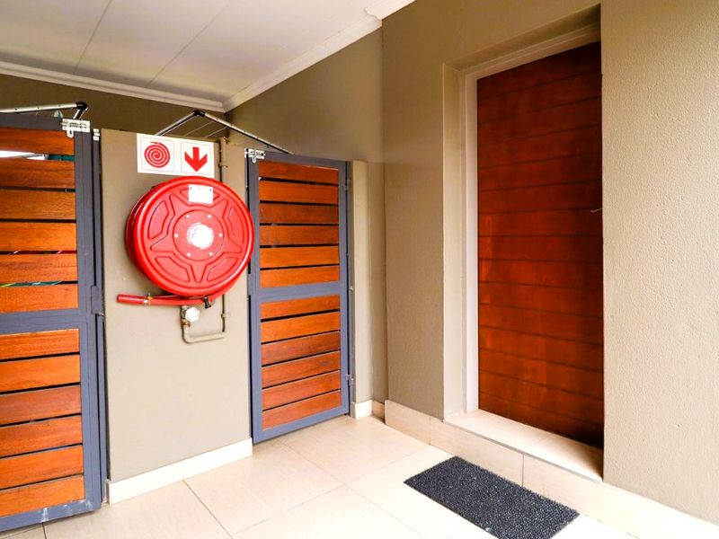 A clean utility area featuring a wall-mounted fire hose reel, timber slat gates, and a solid timber entrance door with tiled flooring.