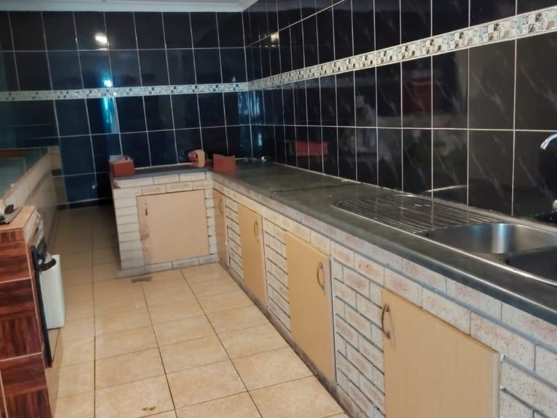 A functional kitchen featuring brick-built cabinetry, a stainless steel sink, and dark tiled splashbacks with ceramic floor tiles.