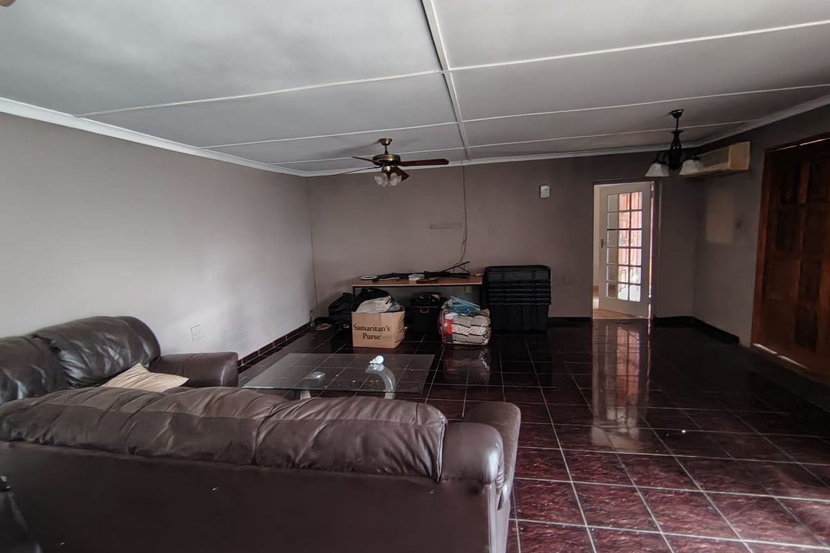Spacious living area featuring dark tiled flooring, a ceiling fan, and an air conditioning unit, with access to an adjacent room via a french door.