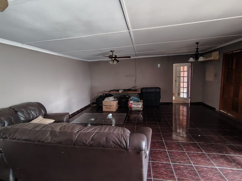 Spacious living area featuring dark tiled flooring, a ceiling fan, and an air conditioning unit, with access to an adjacent room via a french door.