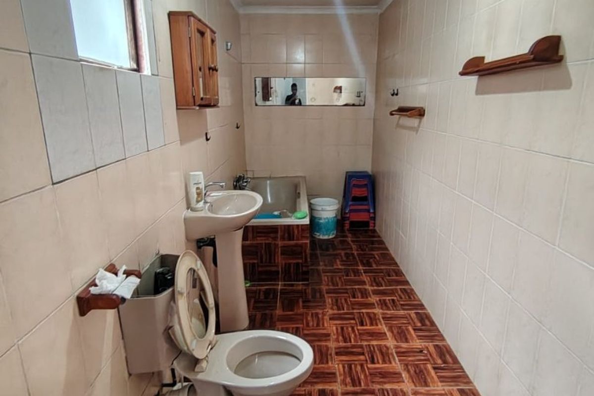 A dated bathroom featuring a pedestal basin, toilet, and built-in bathtub with full-height wall tiling and patterned floor tiles.