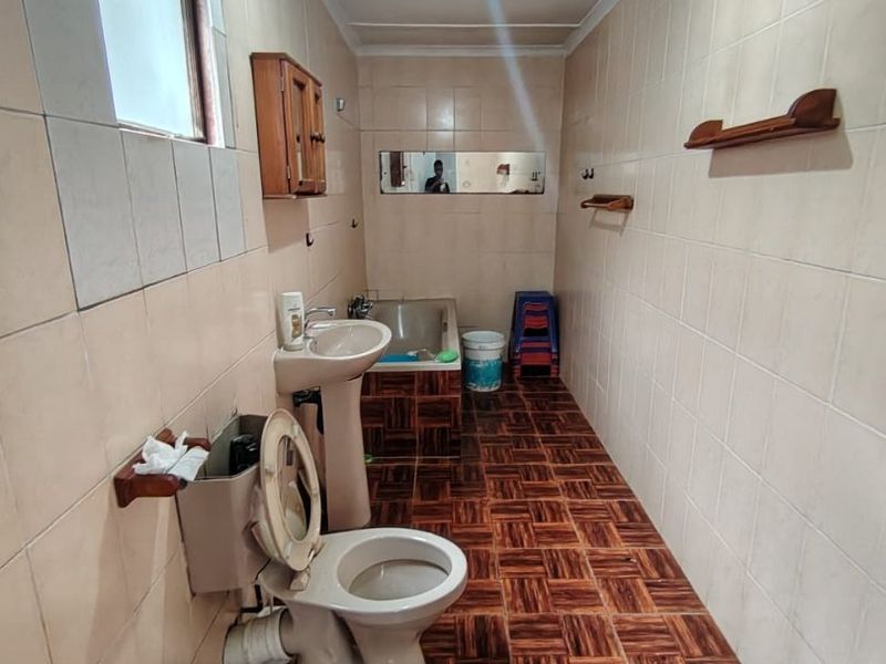 A dated bathroom featuring a pedestal basin, toilet, and built-in bathtub with full-height wall tiling and patterned floor tiles.