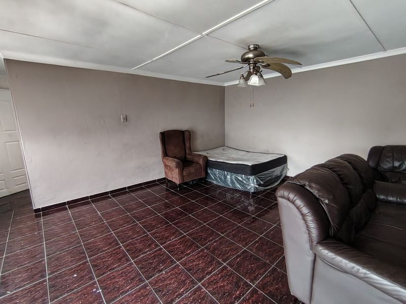 A living area featuring dark tiled flooring and a ceiling fan, requiring cosmetic updates to the ceiling and wall finishes.