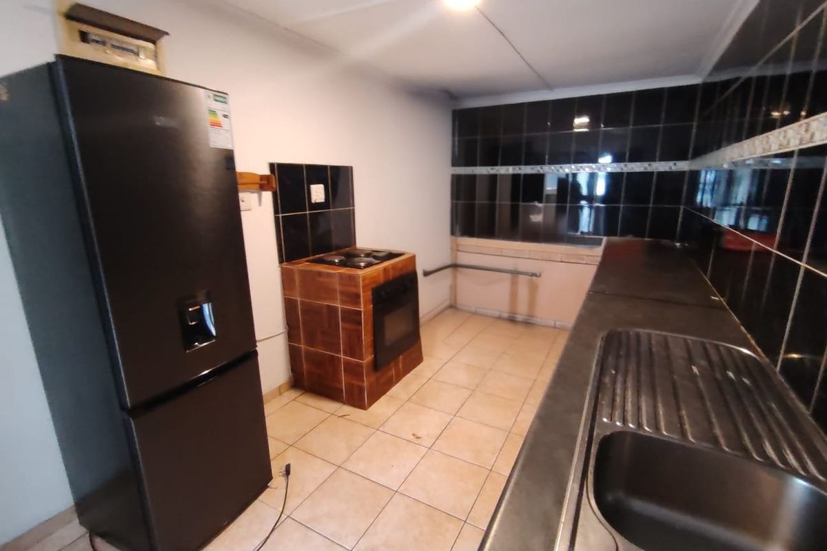 A functional kitchen featuring tiled flooring, a built-in oven with hob, and a stainless steel sink with dark tiled splashbacks.