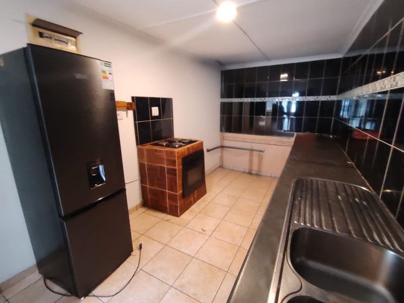 A functional kitchen featuring tiled flooring, a built-in oven with hob, and a stainless steel sink with dark tiled splashbacks.