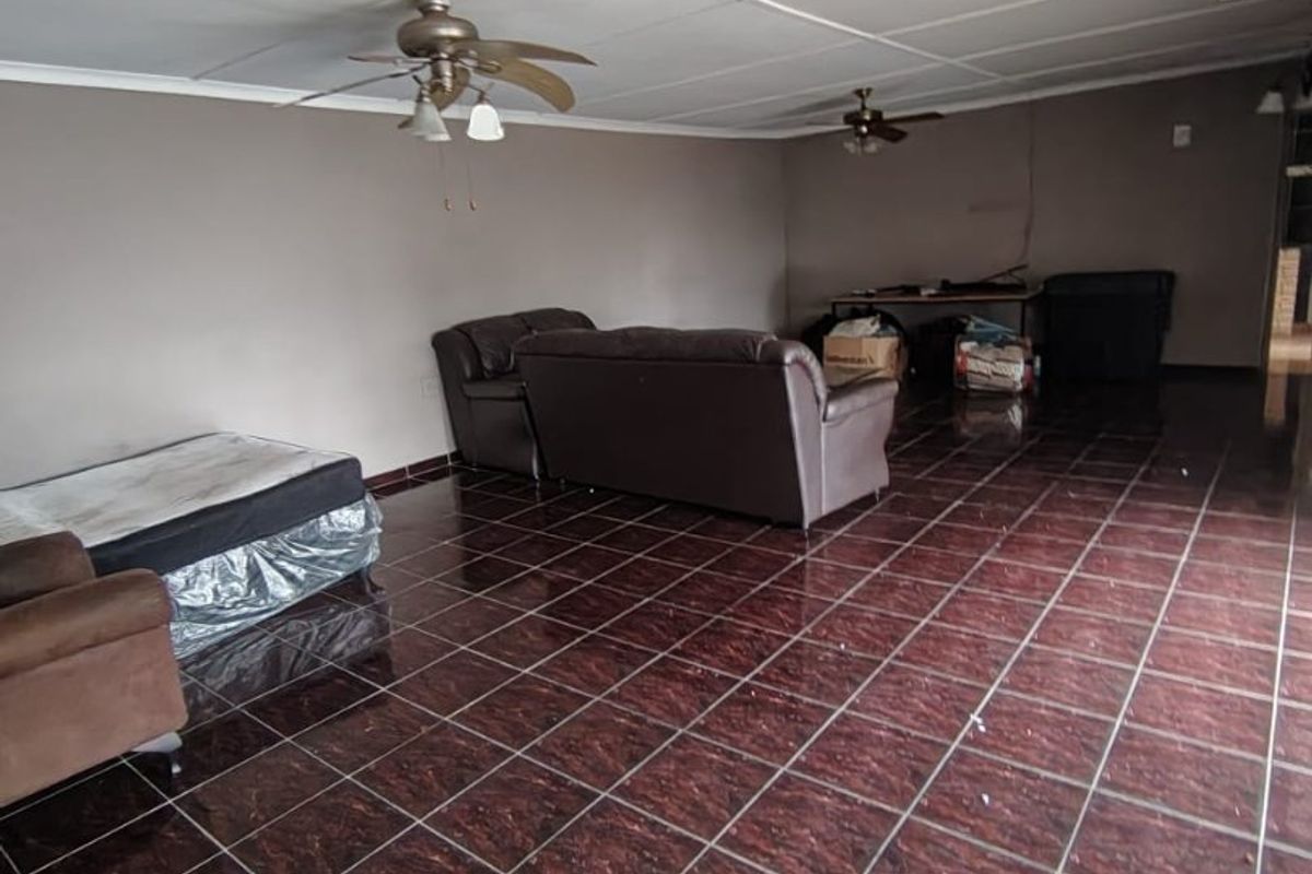 Spacious living area featuring dark tiled flooring and dual ceiling fans, offering a blank canvas for renovation and interior design updates.