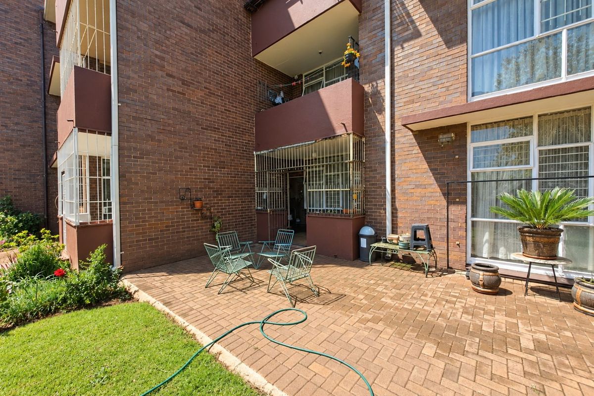 A rear exterior view of the apartment building featuring a paved patio area, brick facade, and access to the unit through sliding glass doors.