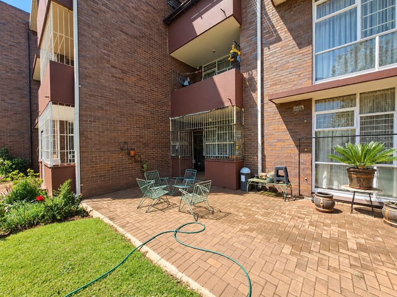 A rear exterior view of the apartment building featuring a paved patio area, brick facade, and access to the unit through sliding glass doors.