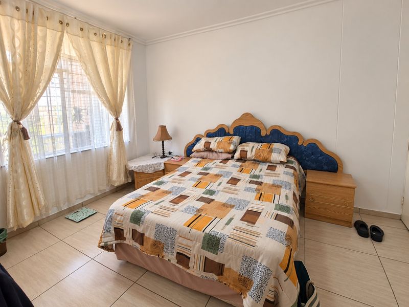 A well-lit bedroom featuring neutral tiled flooring, coving, and a window fitted with security bars.