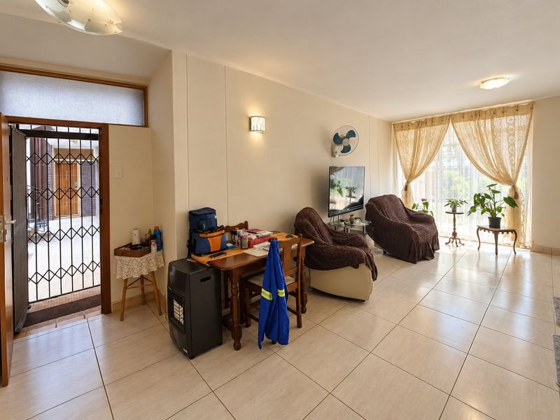 A spacious living area featuring neutral tiled flooring, wall-mounted lighting, and direct access to an outdoor area through a secure sliding glass door.