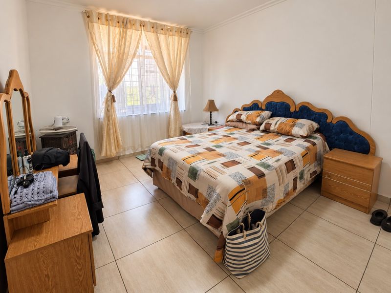 A bedroom featuring tiled flooring and a window fitted with security bars, providing a functional and well-lit living space.