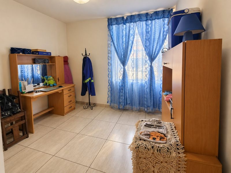 A bedroom featuring neutral tiled flooring and a window with blue curtains, providing a functional space for rest or study.