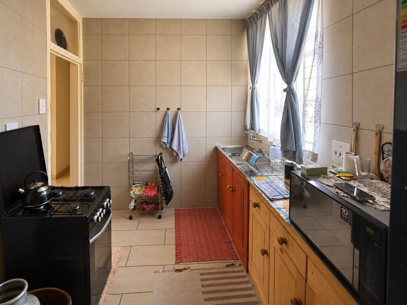 A functional kitchen featuring tiled walls and flooring, built-in wooden cabinetry, a stainless steel sink, and a gas stove.