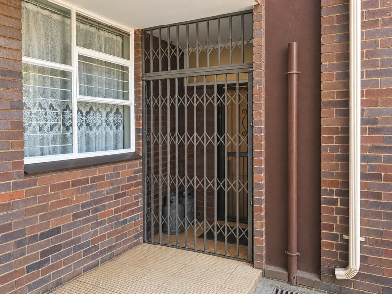 A secure apartment entrance featuring a metal security gate, brick exterior walls, and tiled flooring.