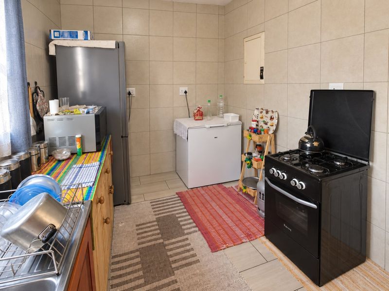A functional kitchen featuring tiled walls and flooring, equipped with a freestanding gas stove and built-in cabinetry with a stainless steel sink.