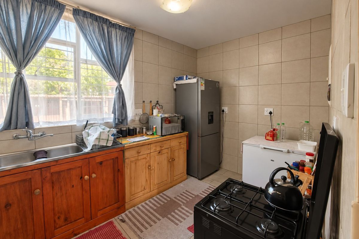 A functional kitchen featuring wooden cabinetry, a double basin sink, tiled splashbacks, and a gas stove, offering a practical layout with natural light.