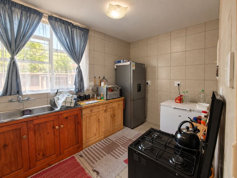 A functional kitchen featuring wooden cabinetry, a double basin sink, tiled splashbacks, and a gas stove, offering a practical layout with natural light.