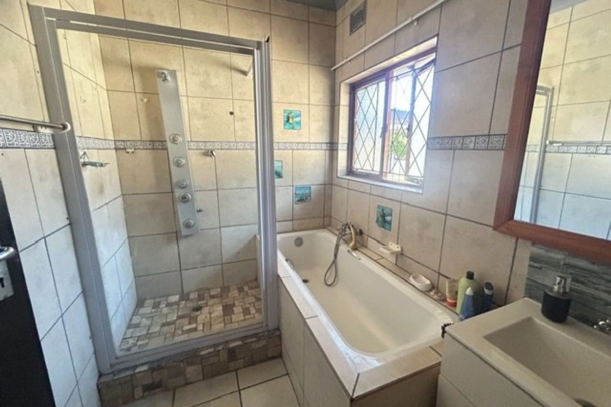 A functional bathroom featuring a separate shower enclosure with a shower panel, a bathtub, and a vanity unit with tiled finishes throughout.