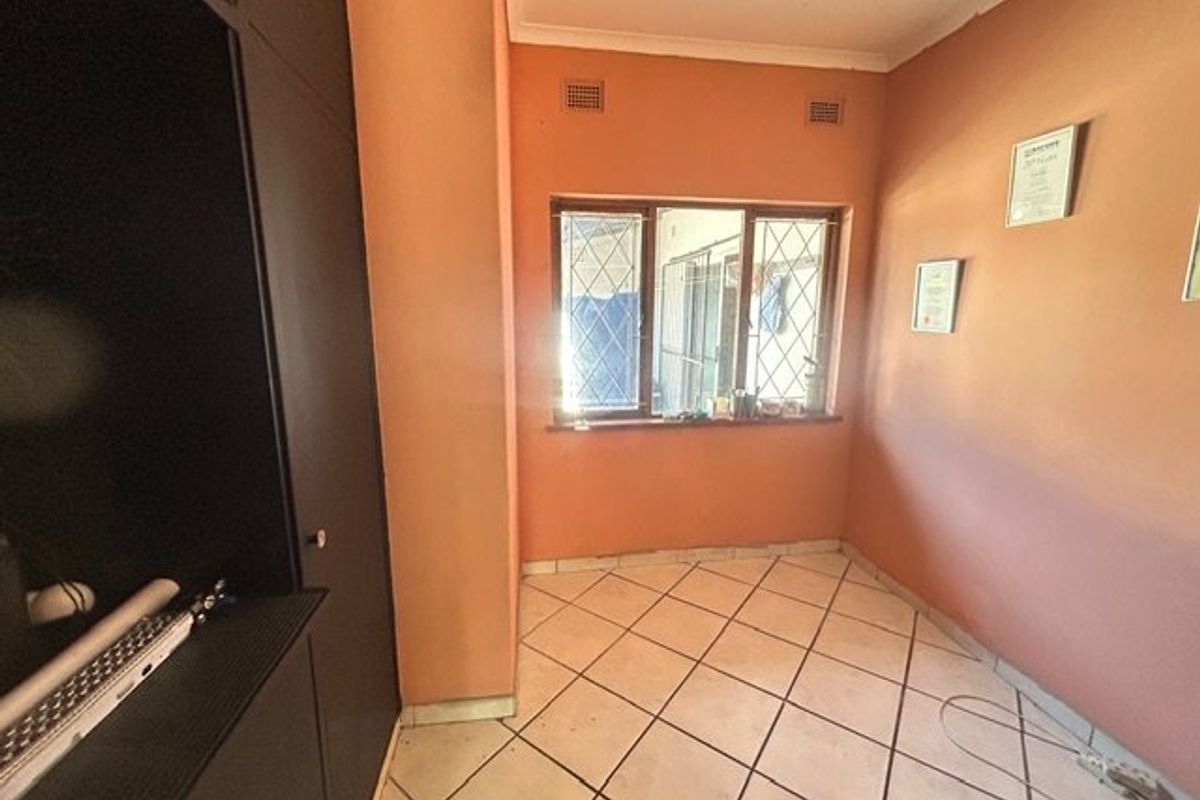 A compact bedroom featuring tiled flooring, built-in cupboards, and security bars on the window, offering a blank canvas for renovation.