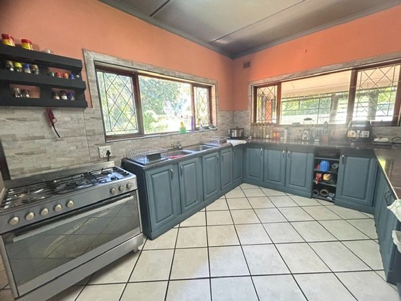 Spacious kitchen featuring blue cabinetry, a gas stove, double sink, and large windows with leaded glass detailing, offering a functional layout.