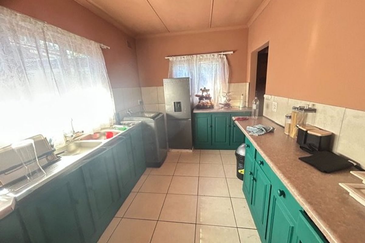 A functional kitchen featuring green built-in cabinetry, laminate countertops, a double basin sink, and tiled flooring with a neutral splashback.