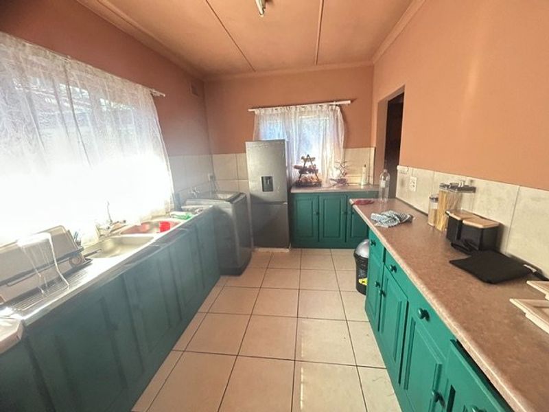 A functional kitchen featuring green built-in cabinetry, laminate countertops, a double basin sink, and tiled flooring with a neutral splashback.