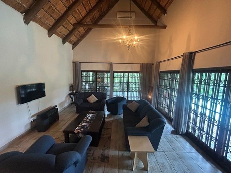 Spacious living room featuring a high vaulted thatched ceiling with exposed timber trusses, ceramic tiled flooring, and large sliding doors with security gates.