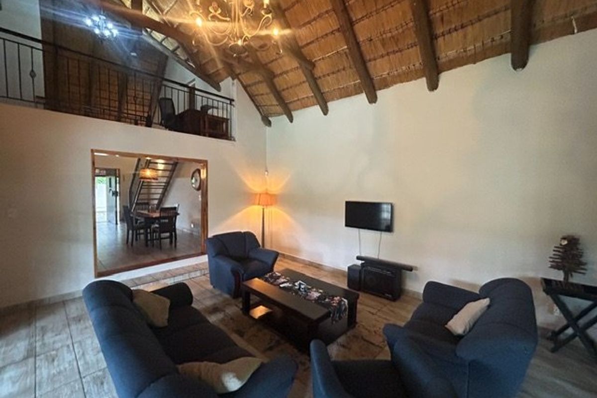 Spacious living room featuring a high vaulted thatched ceiling with exposed timber rafters, tiled flooring, and a mezzanine level with a wrought iron balustrade.