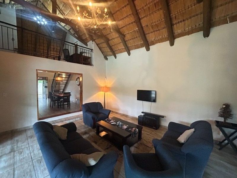 Spacious living room featuring a high vaulted thatched ceiling with exposed timber rafters, tiled flooring, and a mezzanine level with a wrought iron balustrade.