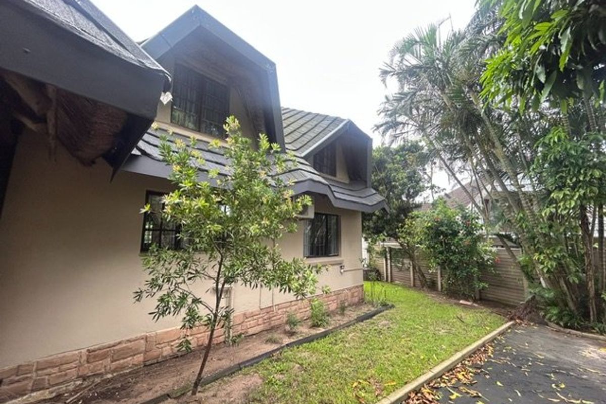 Rear view of the house featuring a tiled roof, dormer windows, and stone cladding accents, set against a landscaped garden and paved driveway.