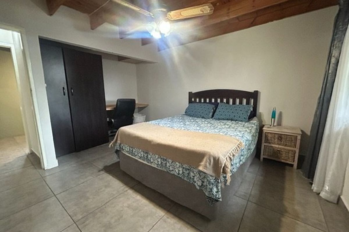 A bedroom featuring tiled flooring, exposed timber ceiling beams, a ceiling fan, and a built-in wardrobe with an integrated desk area.