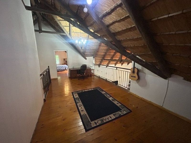 Spacious mezzanine hallway featuring exposed timber rafters, a traditional thatched roof, and polished timber flooring with a metal balustrade overlooking the lower level.
