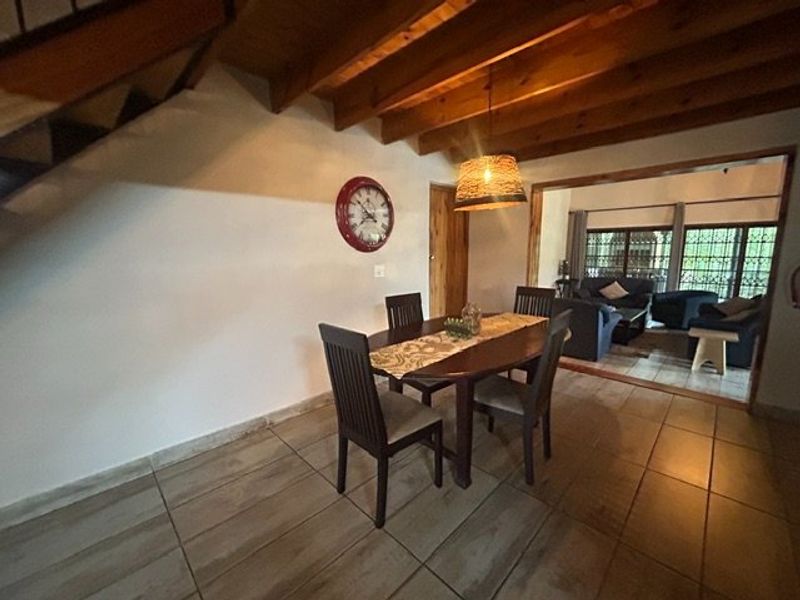 Dining area featuring exposed timber ceiling beams, ceramic floor tiles, and an adjacent living space visible through a large opening.