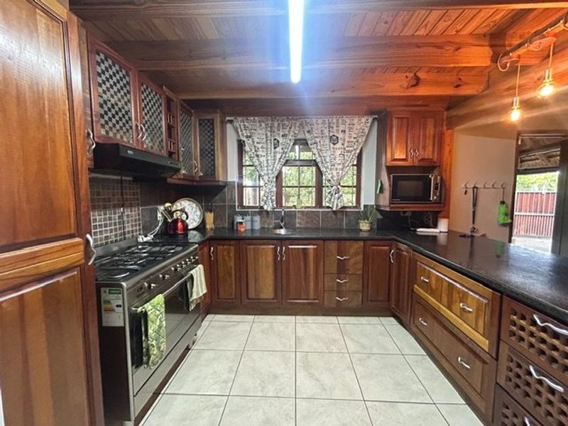 A rustic kitchen featuring extensive wooden cabinetry, granite countertops, a gas stove, and exposed timber ceiling beams with tiled flooring.