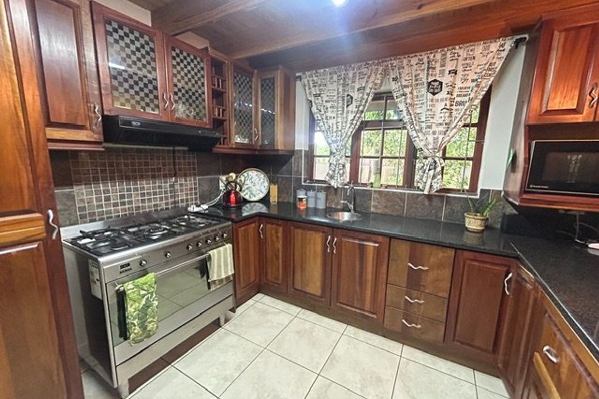 A traditional kitchen featuring warm wooden cabinetry, granite countertops, a gas stove with extractor, and exposed wooden ceiling beams.