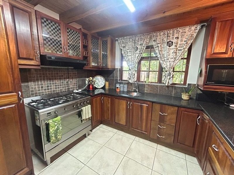A traditional kitchen featuring warm wooden cabinetry, granite countertops, a gas stove with extractor, and exposed wooden ceiling beams.
